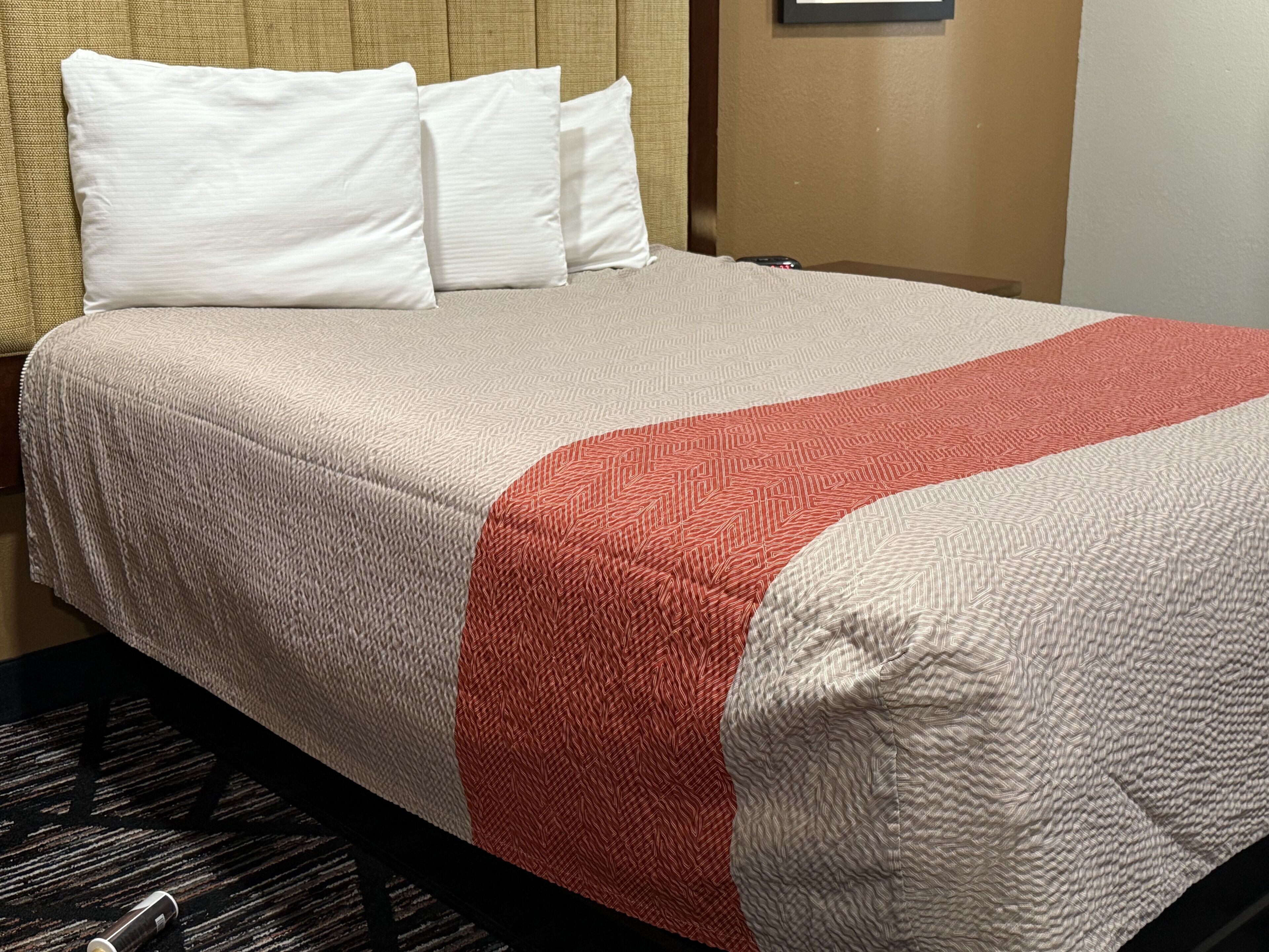 A hotel room with a bed, white pillows, and a red and white patterned bedspread.