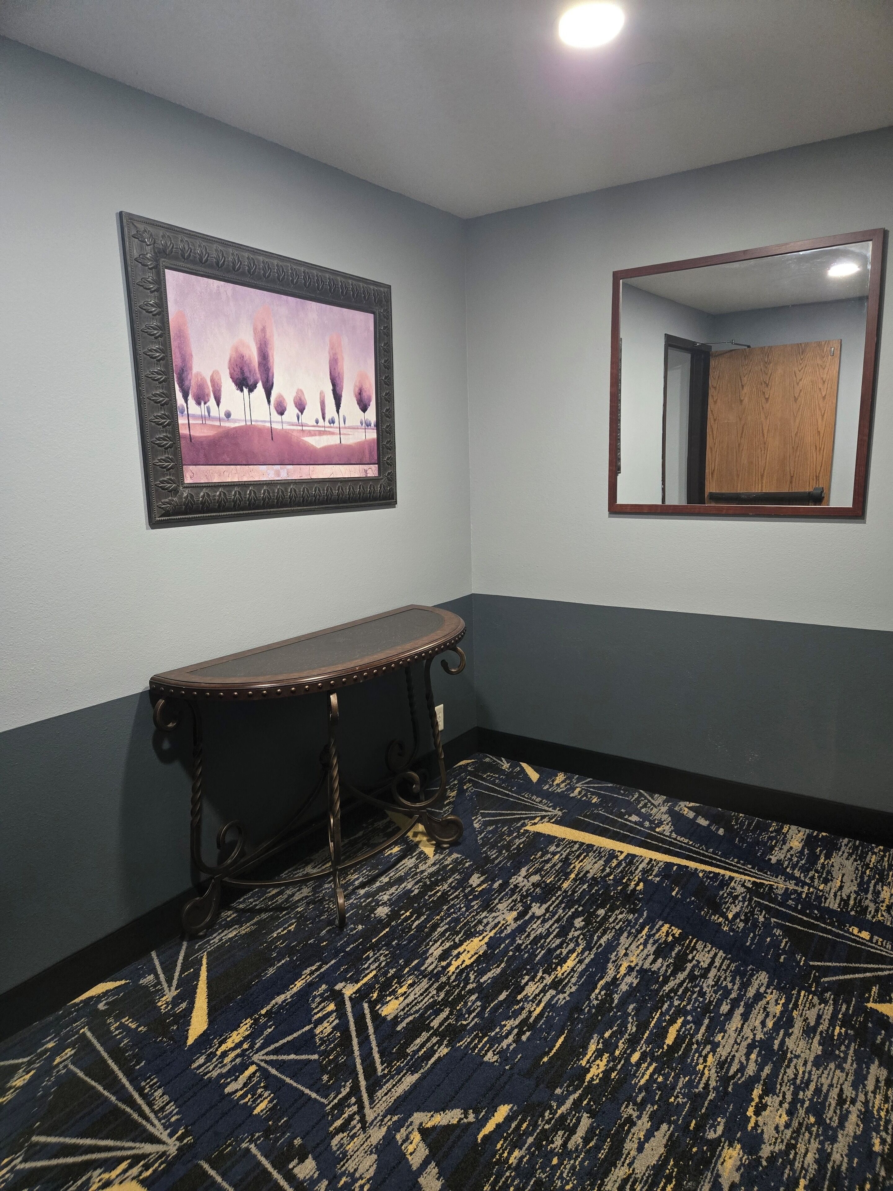 A room with a framed painting, a mirror, a wooden bench, and a patterned carpet.