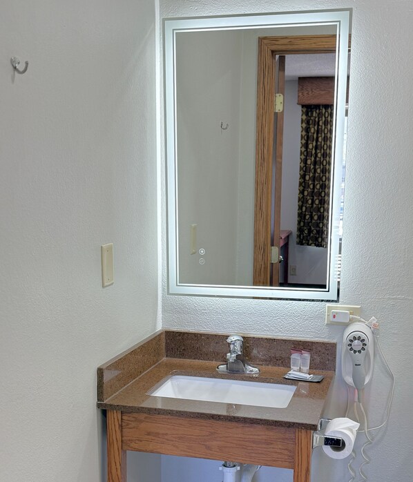 A bathroom with a sink, mirror, and a hairdryer on the wall.