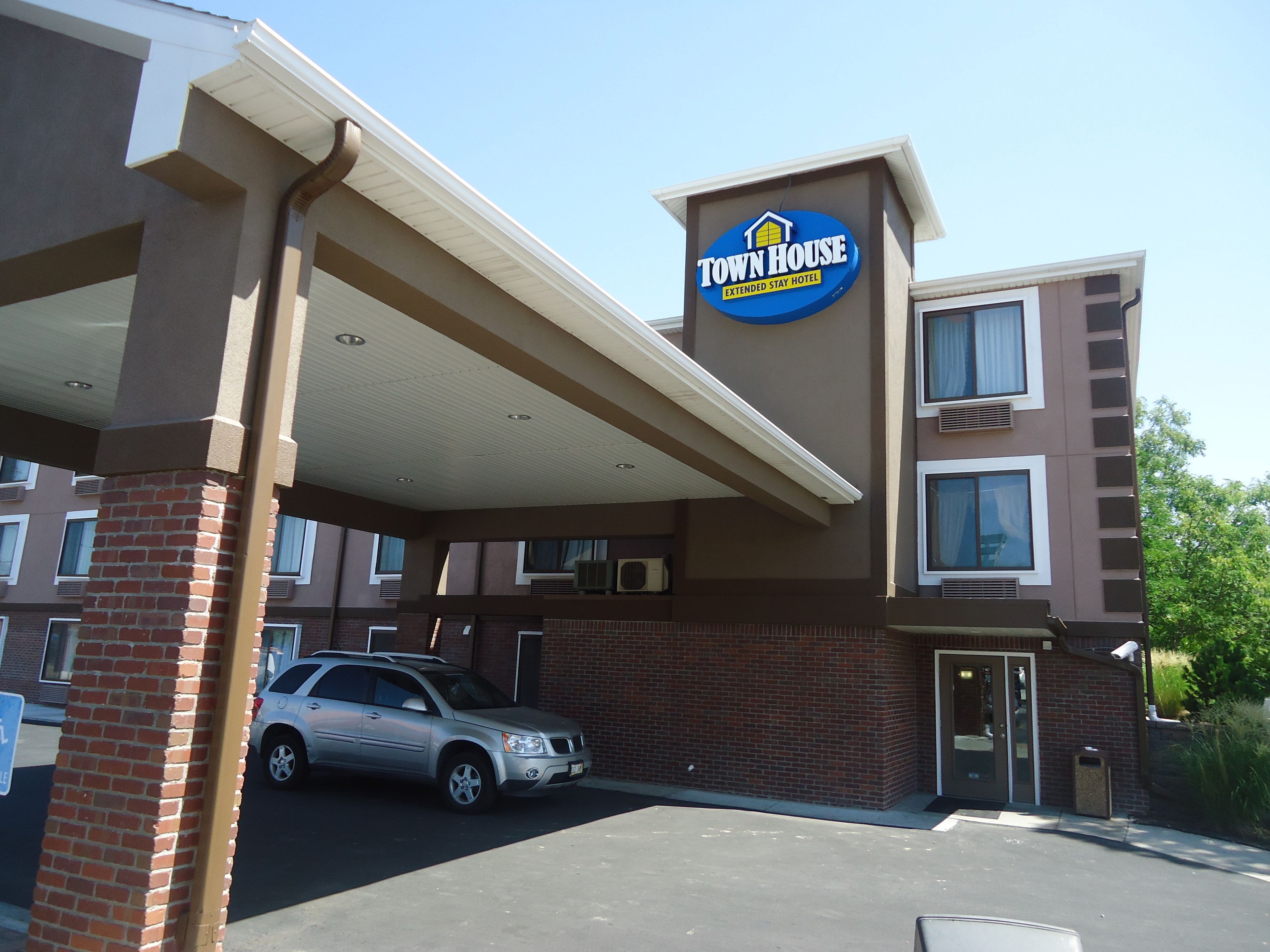 A Town House Extended Stay Hotel with a brick facade, a covered parking area, and a silver car parked in front.