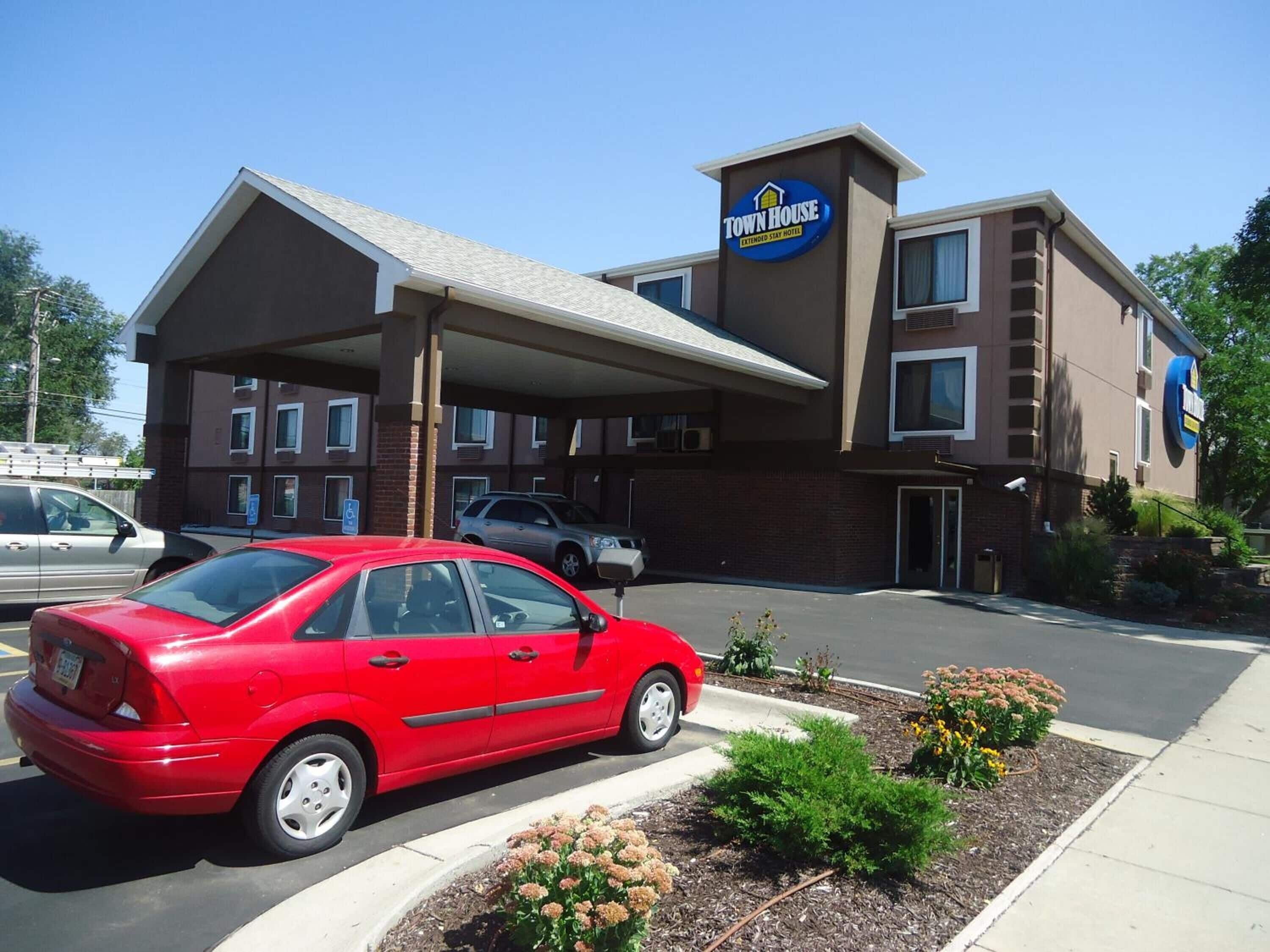 A Town House Extended Stay Hotel with a parking lot, a red car parked in front, and a clear blue sky.