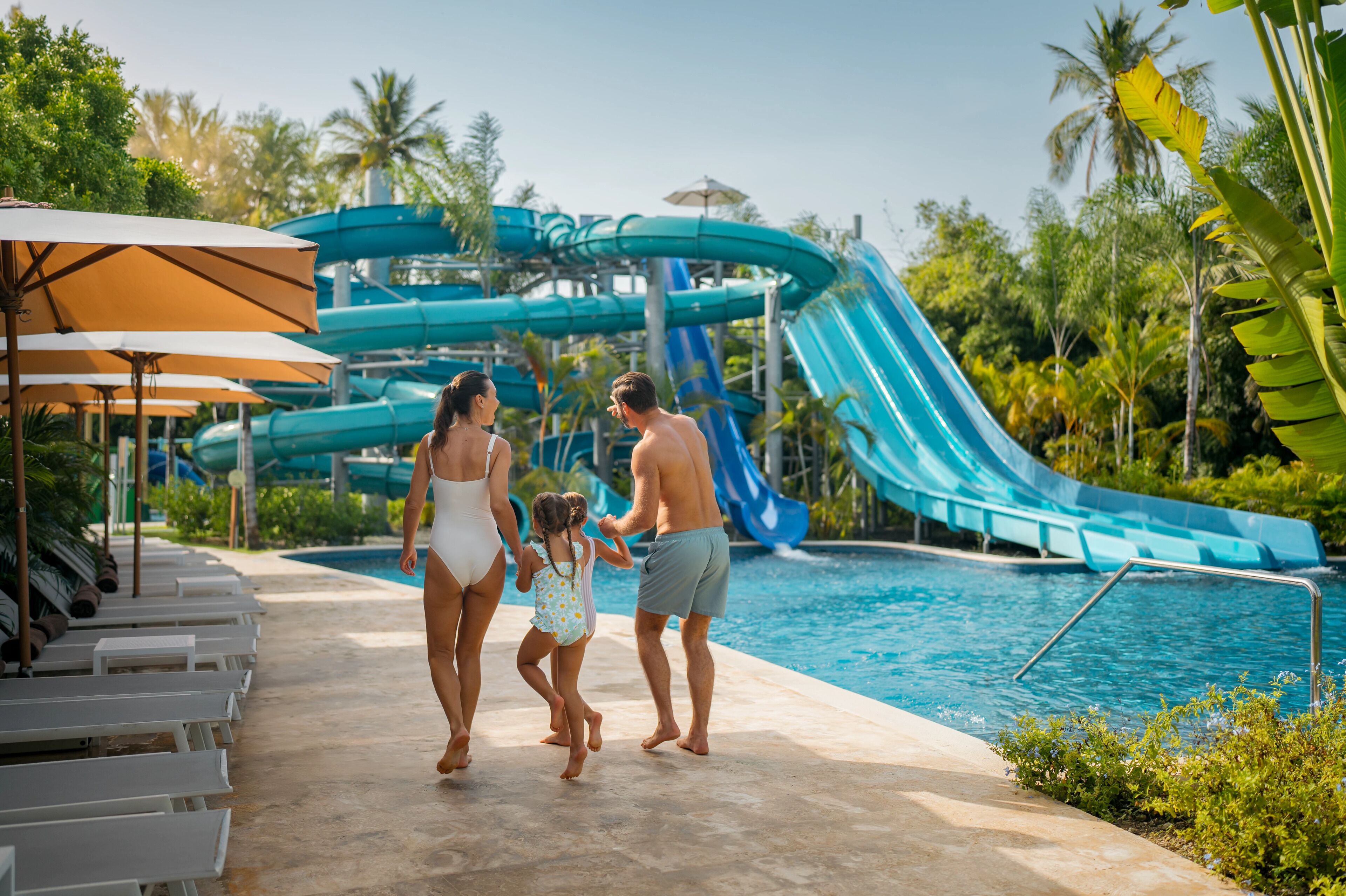 Uma família caminhando perto de uma piscina com um escorregador ao fundo.