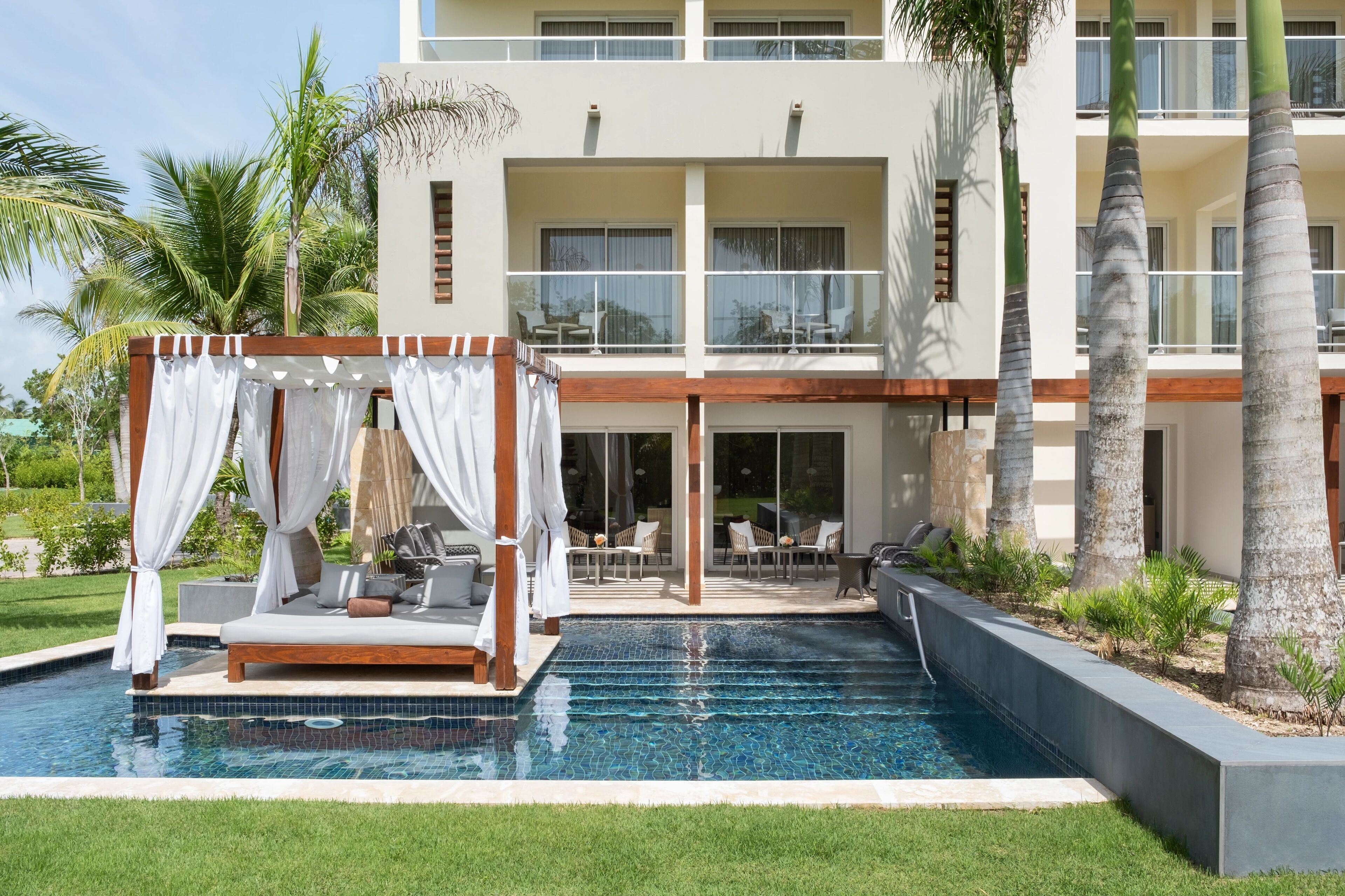 A poolside area with a canopy, lounge chairs, and a view of a multi-story building.