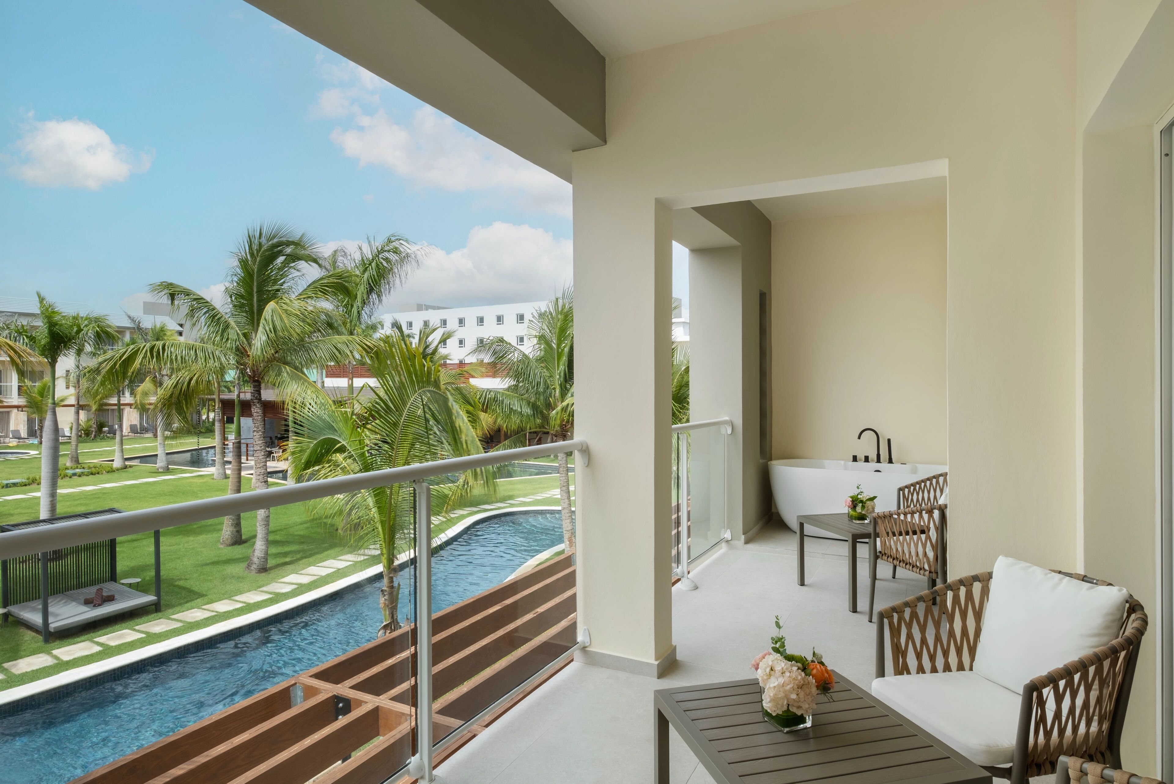 Un balcón con vista a una piscina, una bañera y mobiliario de mimbre.