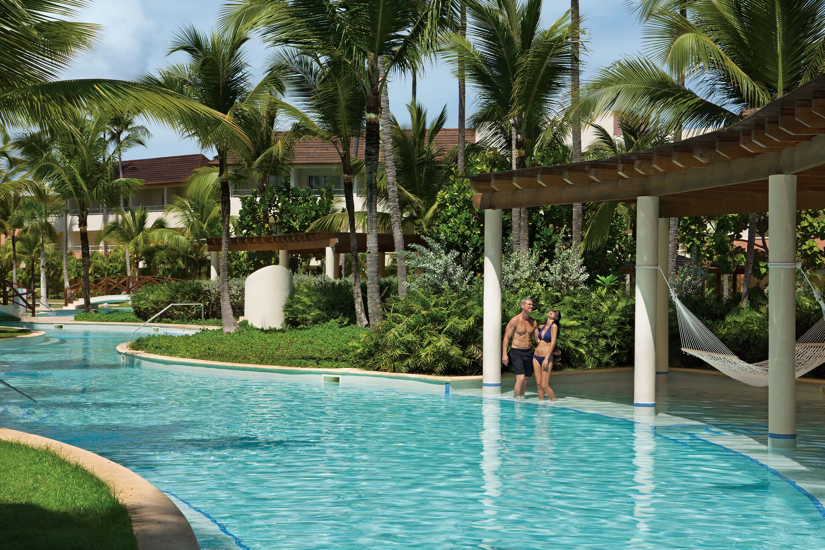 A swimming pool with palm trees and a covered area.