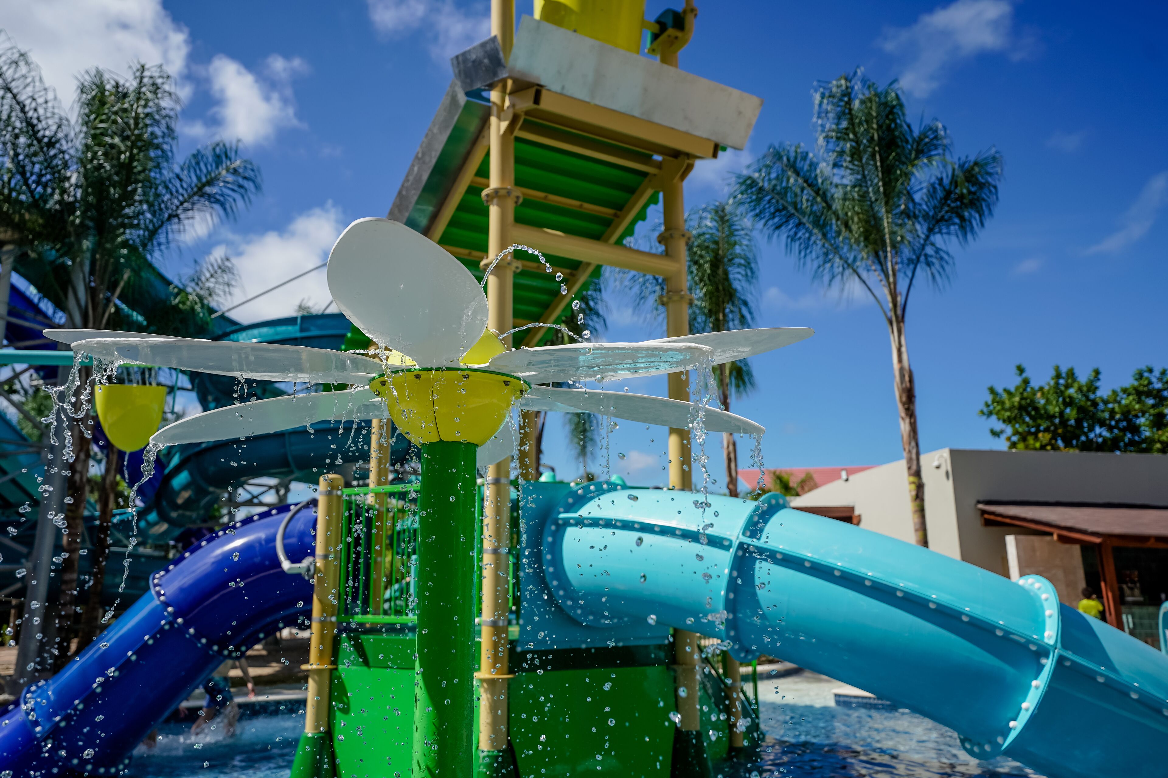 Un parc aquatique avec un toboggan aquatique, une fontaine et des palmiers en arrière-plan.