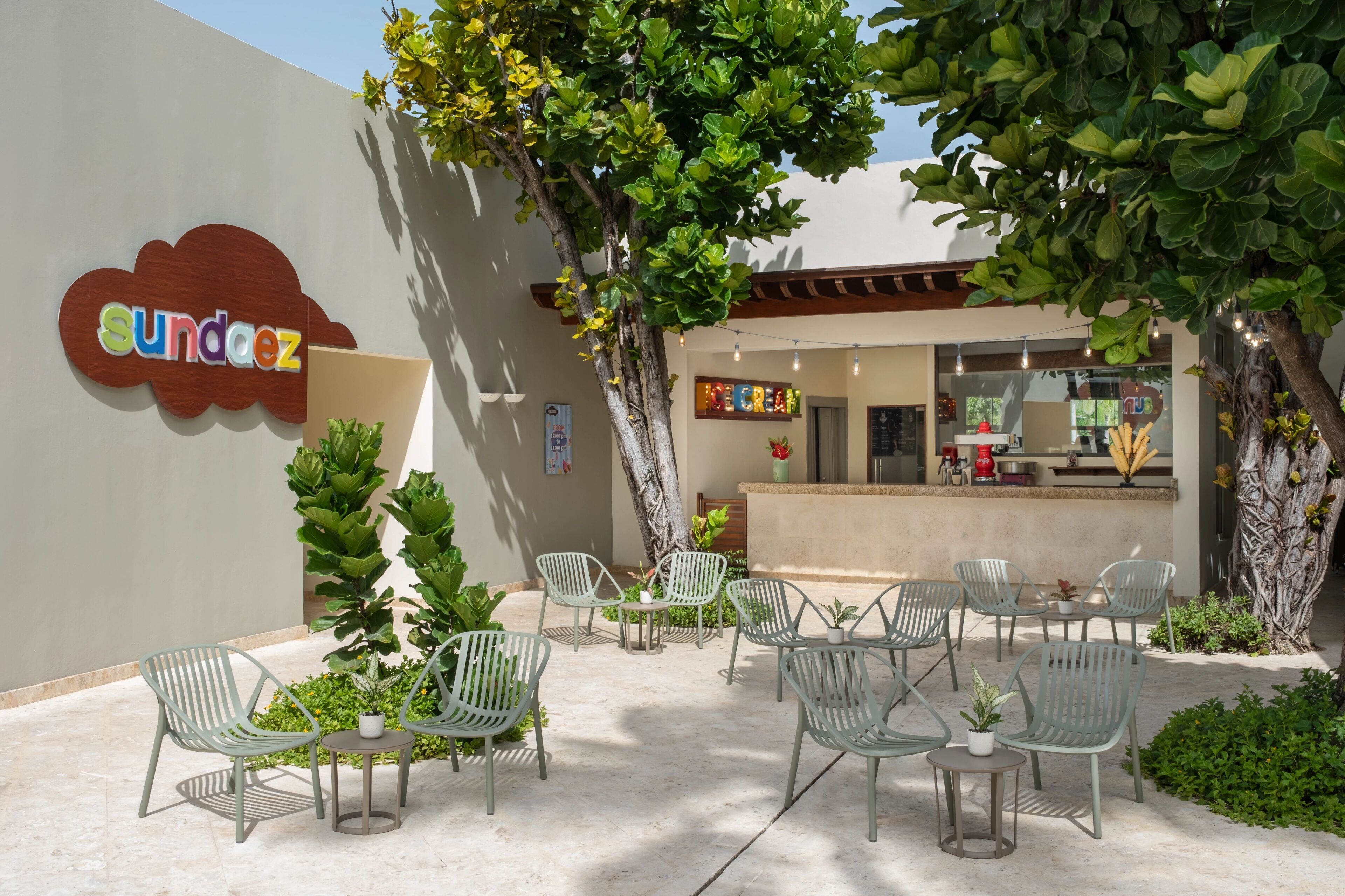 An outdoor seating area with metal chairs and tables, a sign for 'Sundaez', and a restaurant with a counter and hanging lights.
