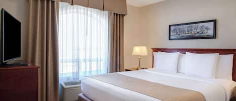Habitación de hotel con una cama grande, un televisor de pantalla plana sobre un soporte de madera, una ventana con cortinas, un cuadro en la pared y una lámpara de noche.