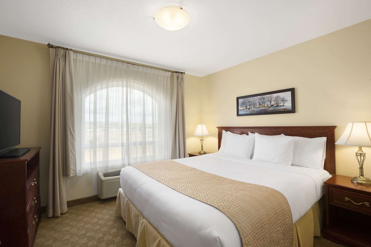 A hotel room with a large bed, a television on a dresser, a painting on the wall, and a window with curtains.