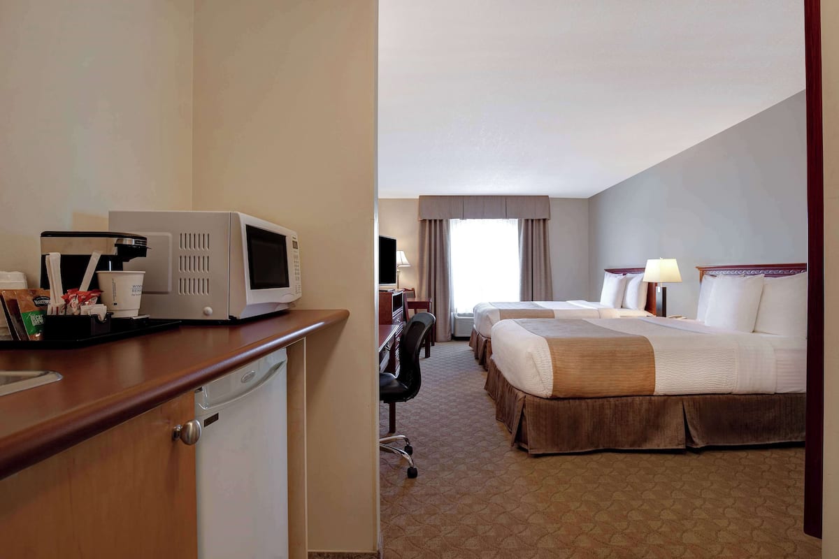 A hotel room with a kitchenette, a bed, a desk, and a chair.