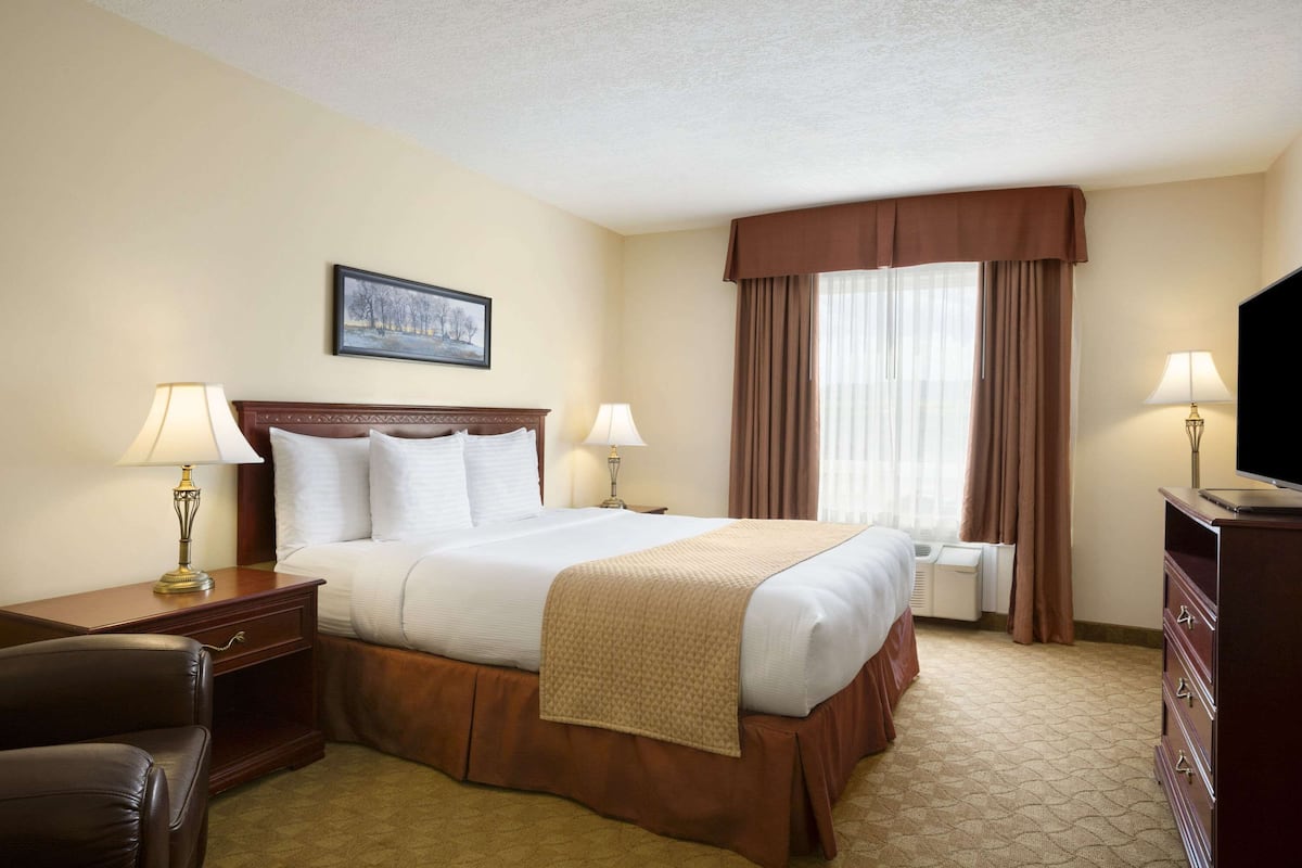A hotel room with a large bed, two bedside tables with lamps, a television, a dresser, and a painting on the wall.