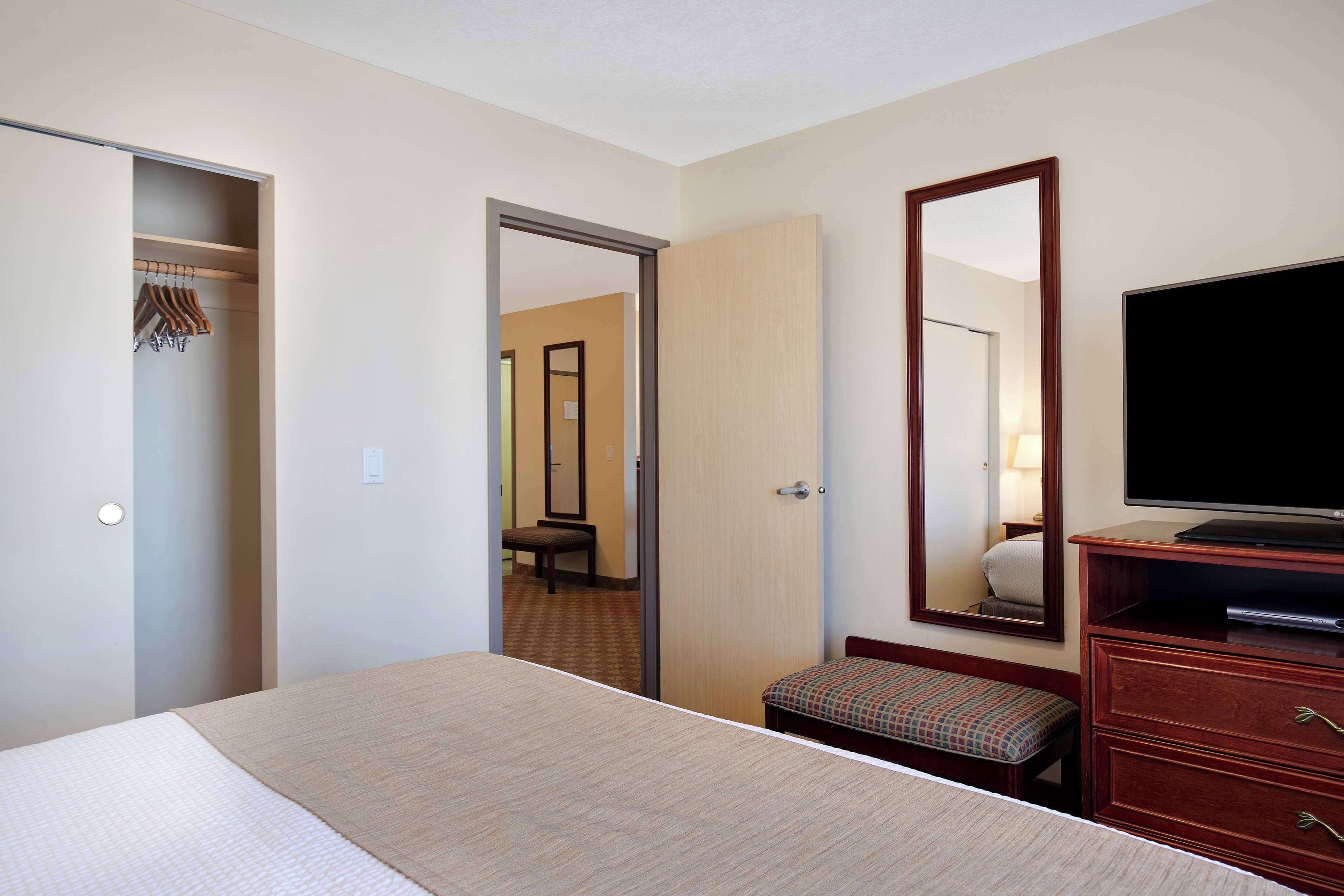 Une chambre d’hôtel équipée d’un lit, d’une télévision, d’un miroir, d’un banc et d’une armoire.