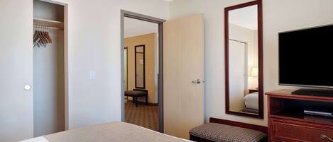Une chambre d’hôtel équipée d’un lit, d’une télévision, d’un miroir, d’un banc et d’une armoire.