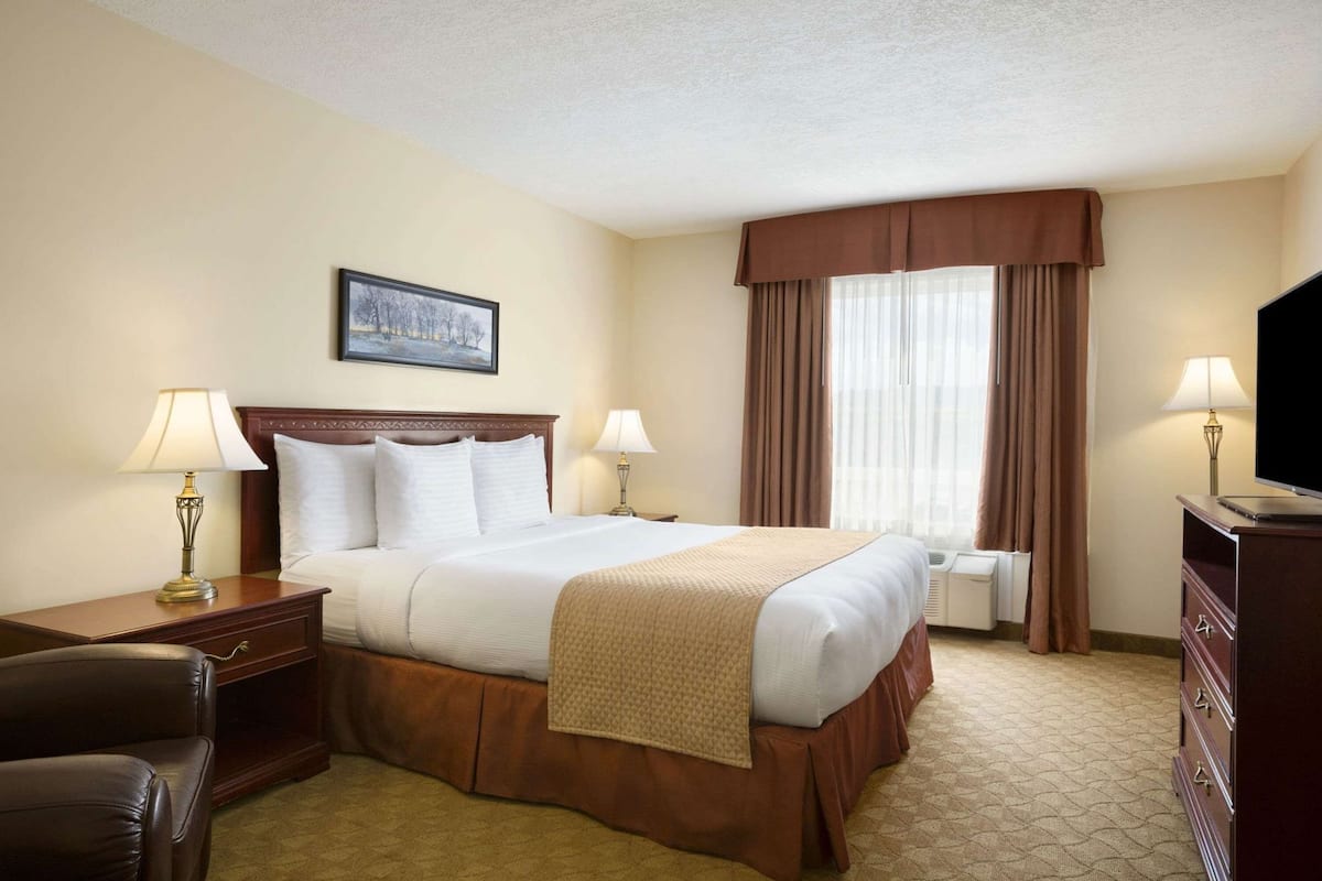 A hotel room with a bed, two bedside tables with lamps, a TV, a chair, and a window with curtains.