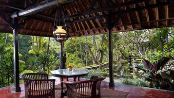 A covered outdoor seating area with a table and chairs, overlooking a pond and lush greenery.