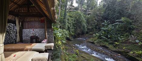 A serene spa area with a stone wall, a small table with a red flower, and a bed with a beige cover.
