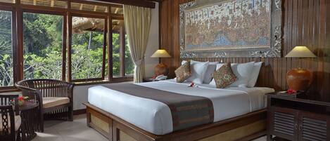 A spacious bedroom with a large bed, two bedside tables, a nightstand, a chair, and a window with a view of greenery.