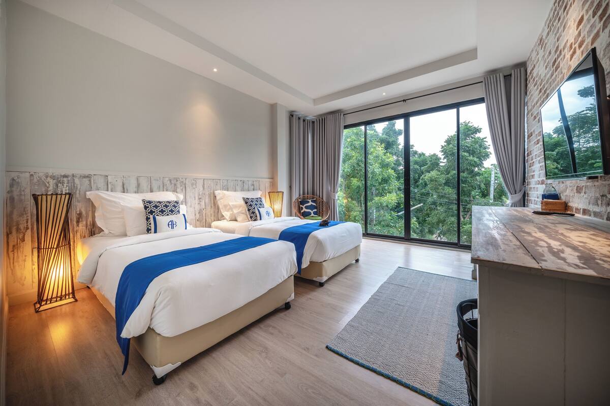 Una habitación de hotel moderna con dos camas, un ventanal grande y vistas a zonas verdes.
