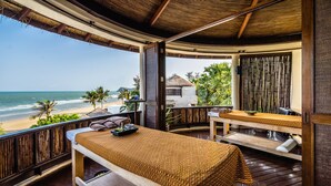 A wooden deck with a massage table, a small table with a plant, and a view of the beach. - Aleenta Hua Hin - Pranburi (Pranburi)