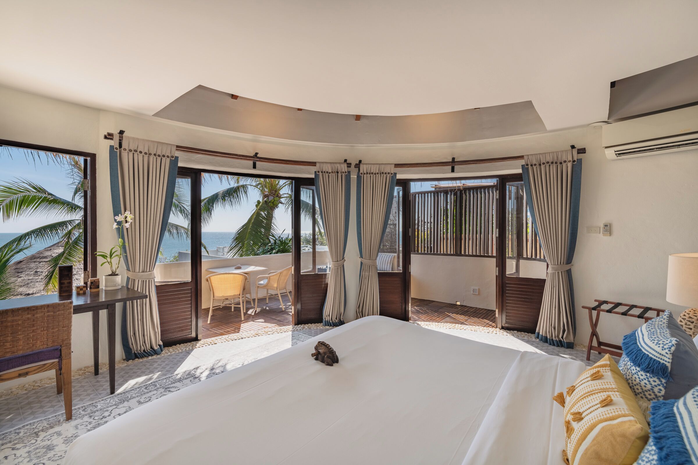 A hotel room with a large bed, a desk, and a view of the beach.