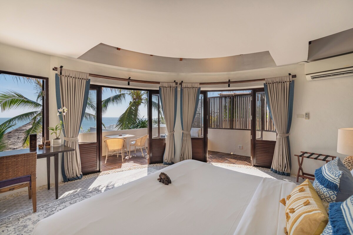 A hotel room with a large bed, a desk, and a view of the beach.