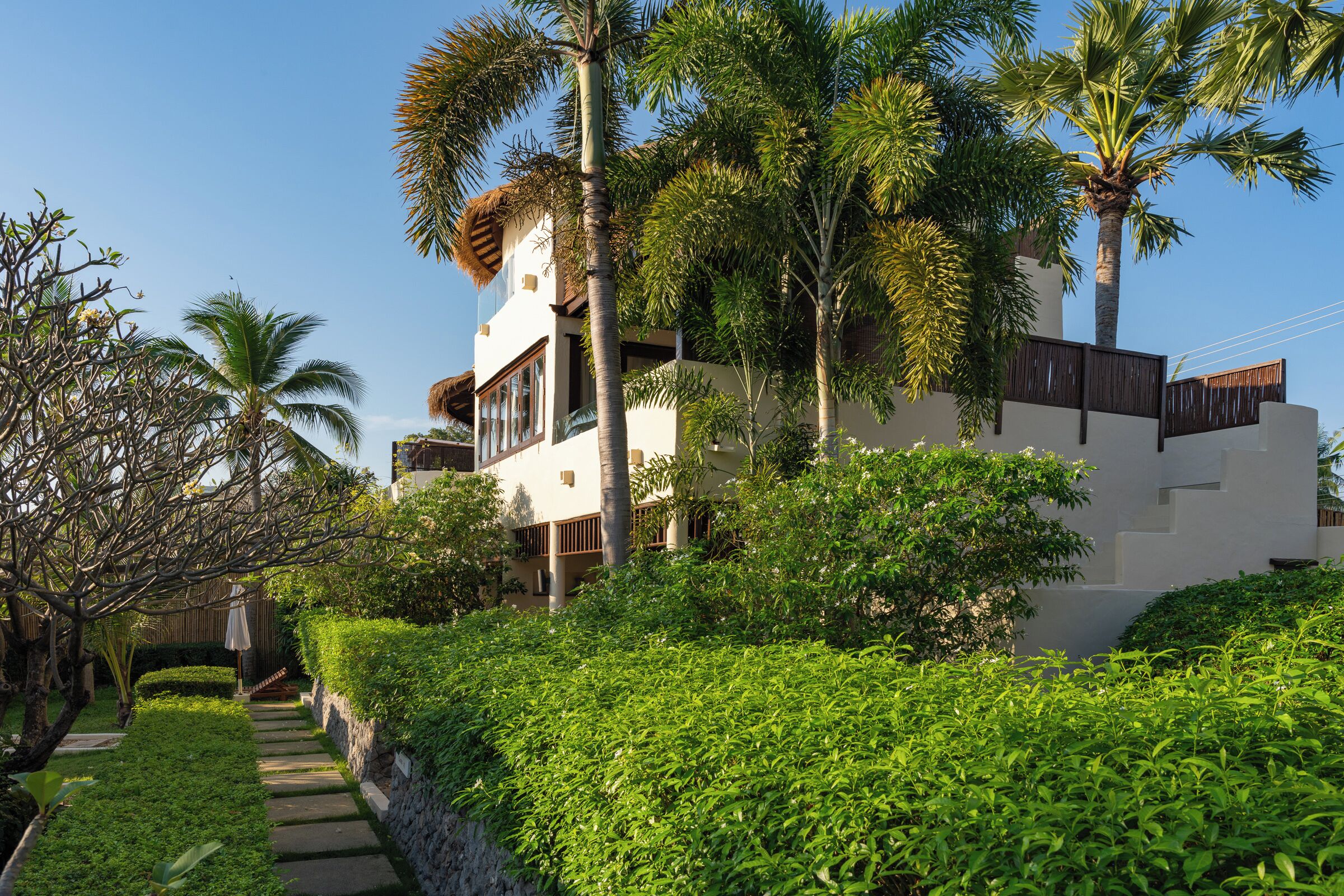Ein modernes Gebäude mit weißer Fassade, umgeben von üppiger Vegetation und Palmen.