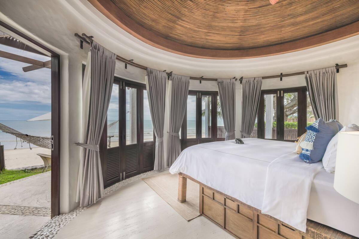 Un dormitorio con una cama grande, cortinas y vista a la playa.