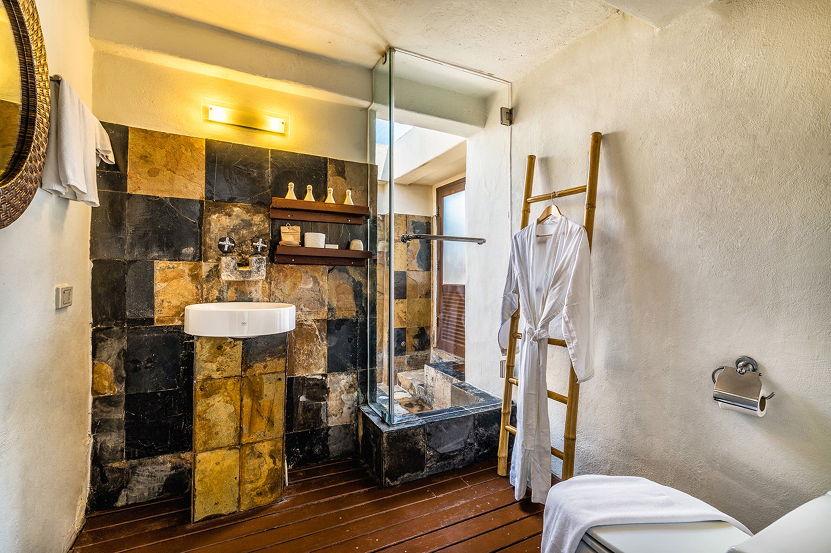 A bathroom with a stone wall, a white sink, a glass-enclosed shower, and a wooden floor.