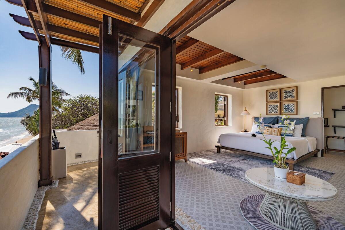 Un dormitorio con una cama grande, una ventana con vista al océano y un balcón con vista a la playa.
