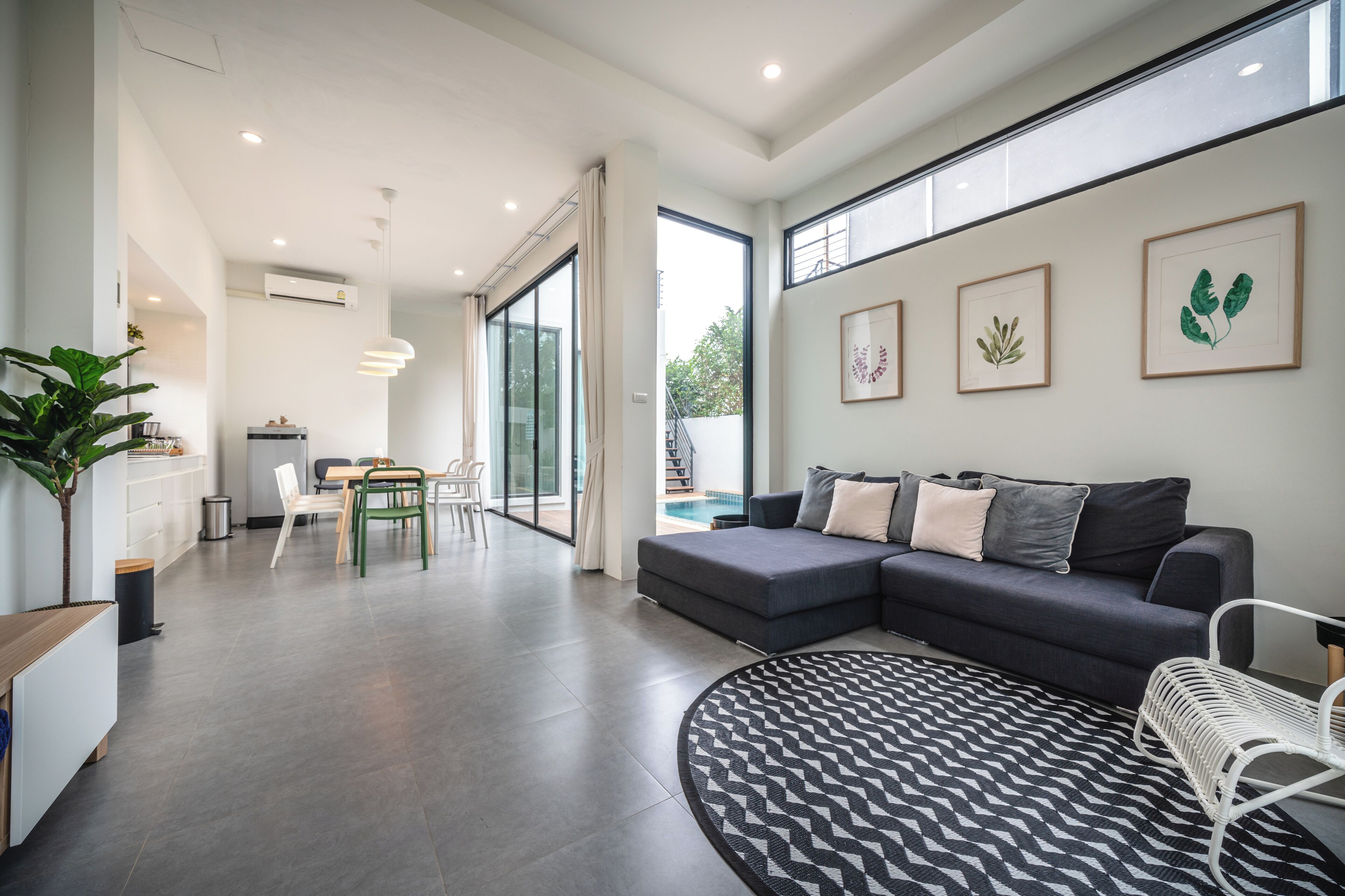 A modern living room with a dark sofa, a patterned rug, and a dining area with chairs and a table.