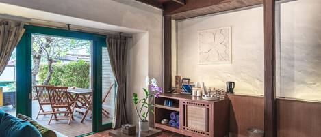 Una habitación acogedora con techo de madera, una zona de comedor con sillas y una mesa, un mueble pequeño con objetos, y vistas a través de un ventanal.