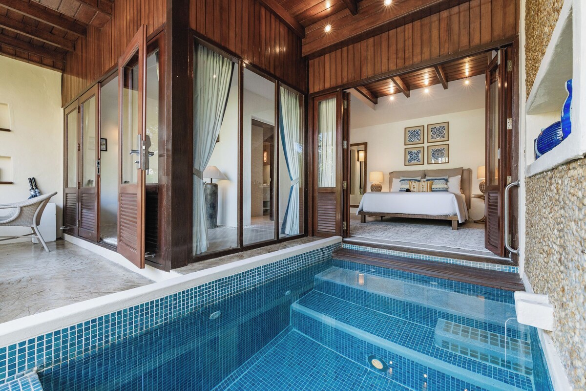 A hotel room with a large window, a bed, a bathroom, and a pool area.