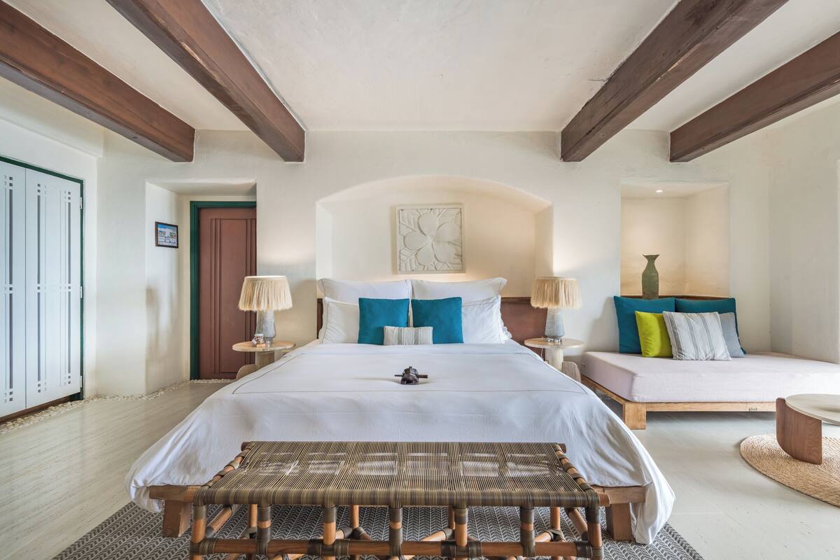 Un dormitorio con una cama grande, un banco, una mesita de noche y un buró.