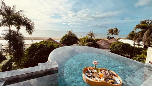 A infinity pool with a breakfast tray in the center, surrounded by palm trees and a beach view. - Aleenta Hua Hin - Pranburi (Pranburi)