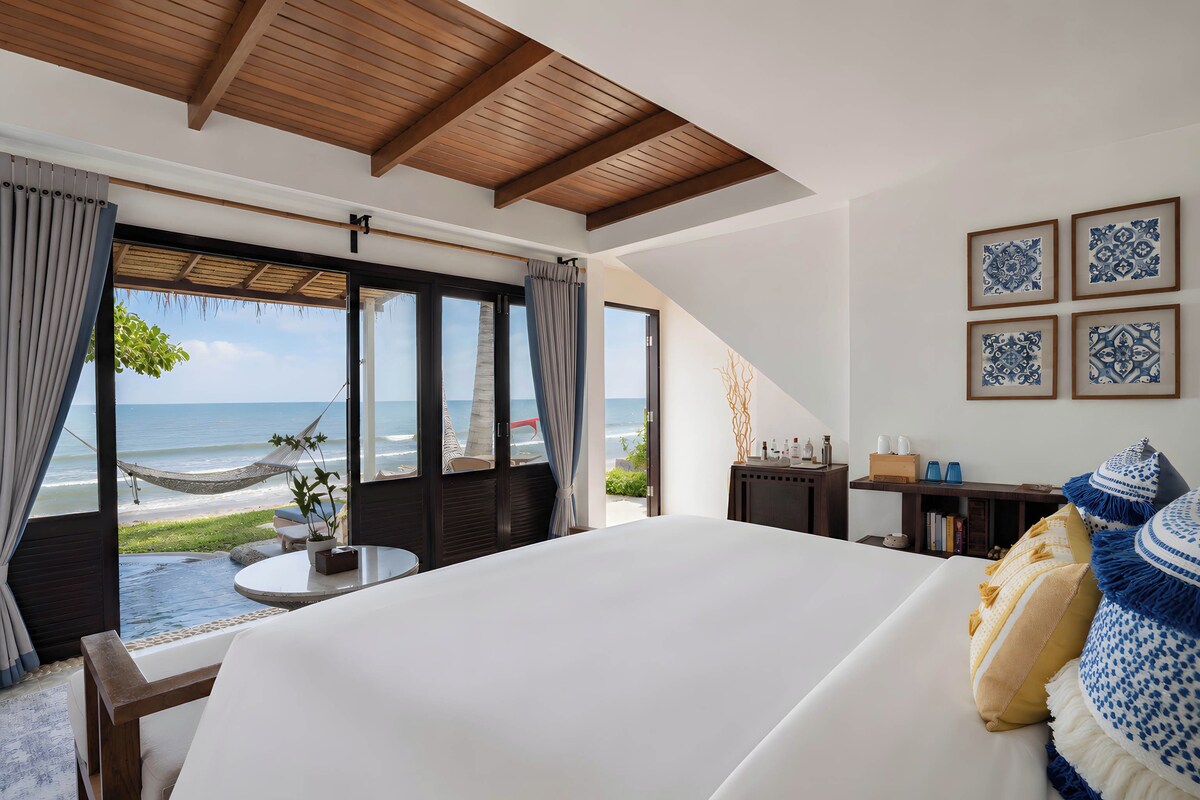 Une chambre dotée d’un grand lit, offrant une vue sur l’océan, et comprenant un coin repas avec une table et des chaises.