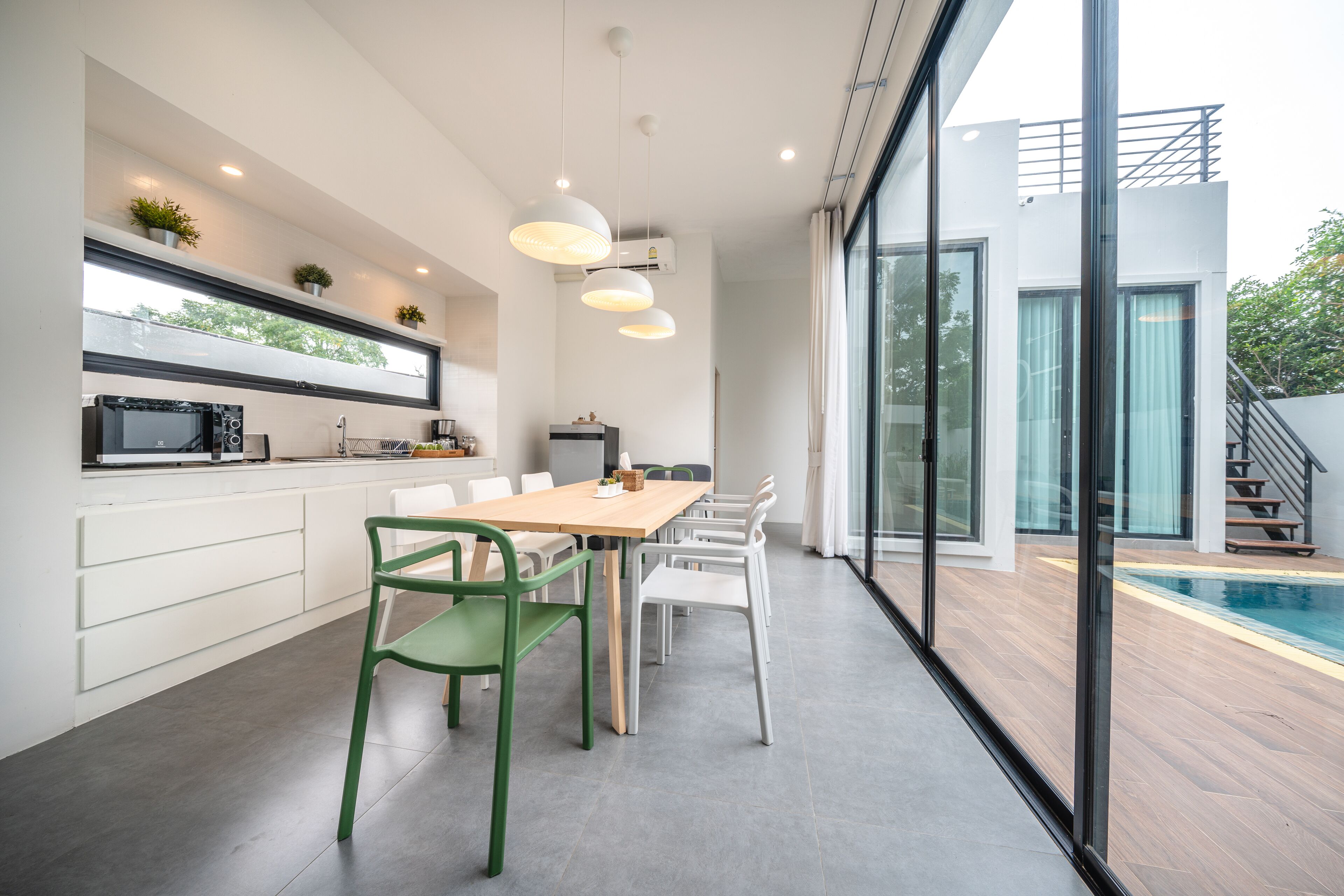 A modern kitchen with a dining area, a pool, and a staircase leading to an upper level.