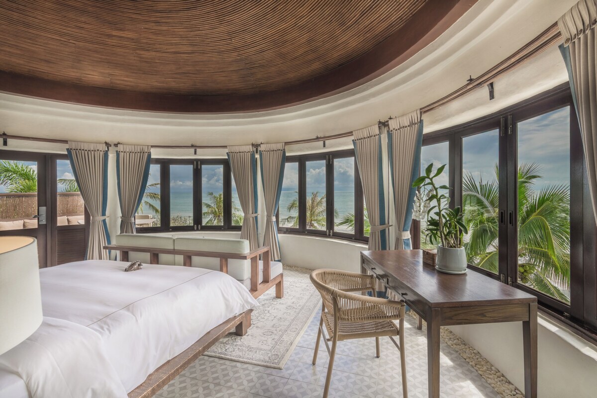 A bedroom with a large bed, a desk, and a view of the ocean.