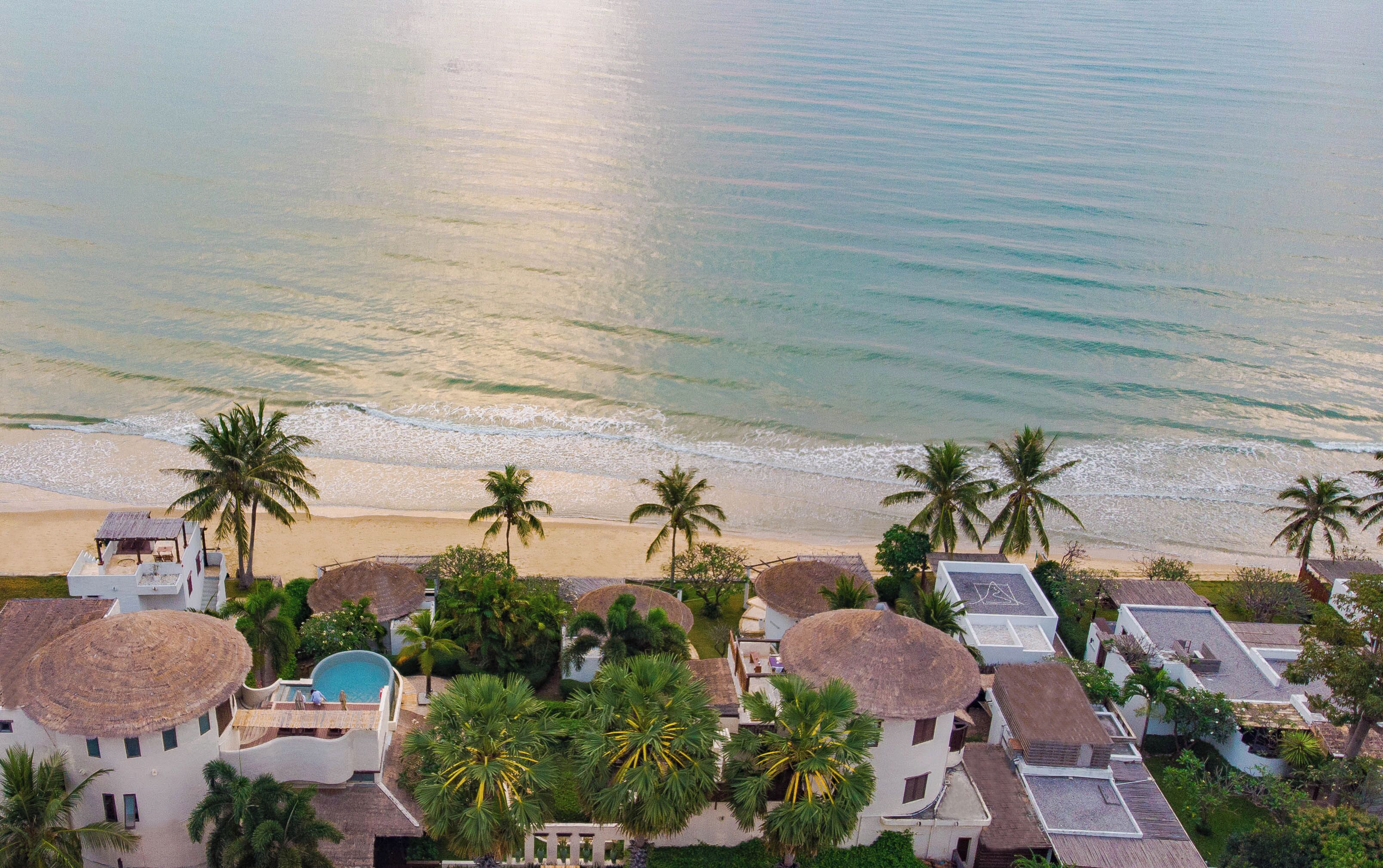 A coastal resort with thatched-roof villas, a swimming pool, and palm trees.