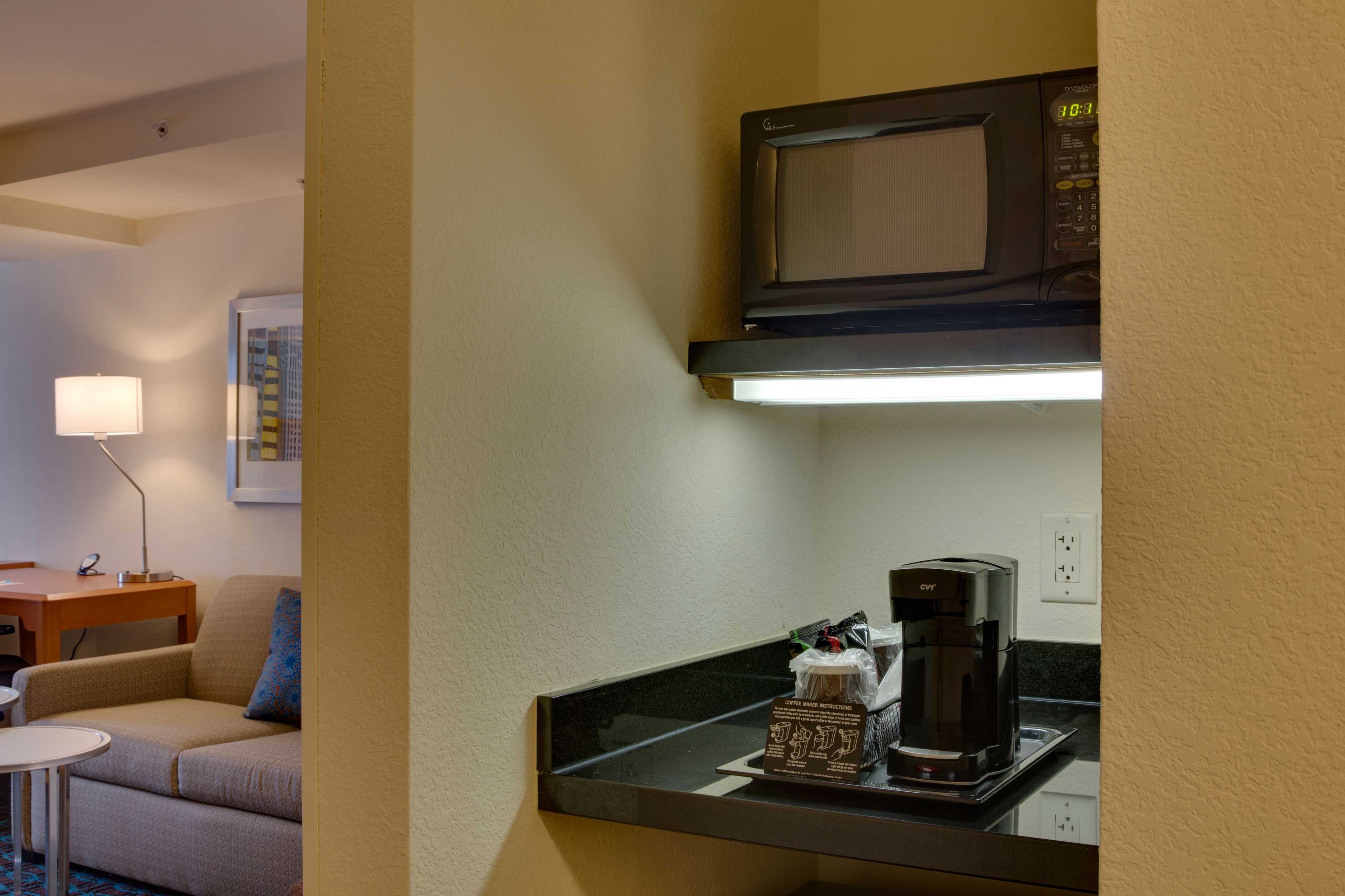 Hotelkamer met kitchenette, inclusief een magnetron, koffiezetapparaat en een tafeltje met lamp.