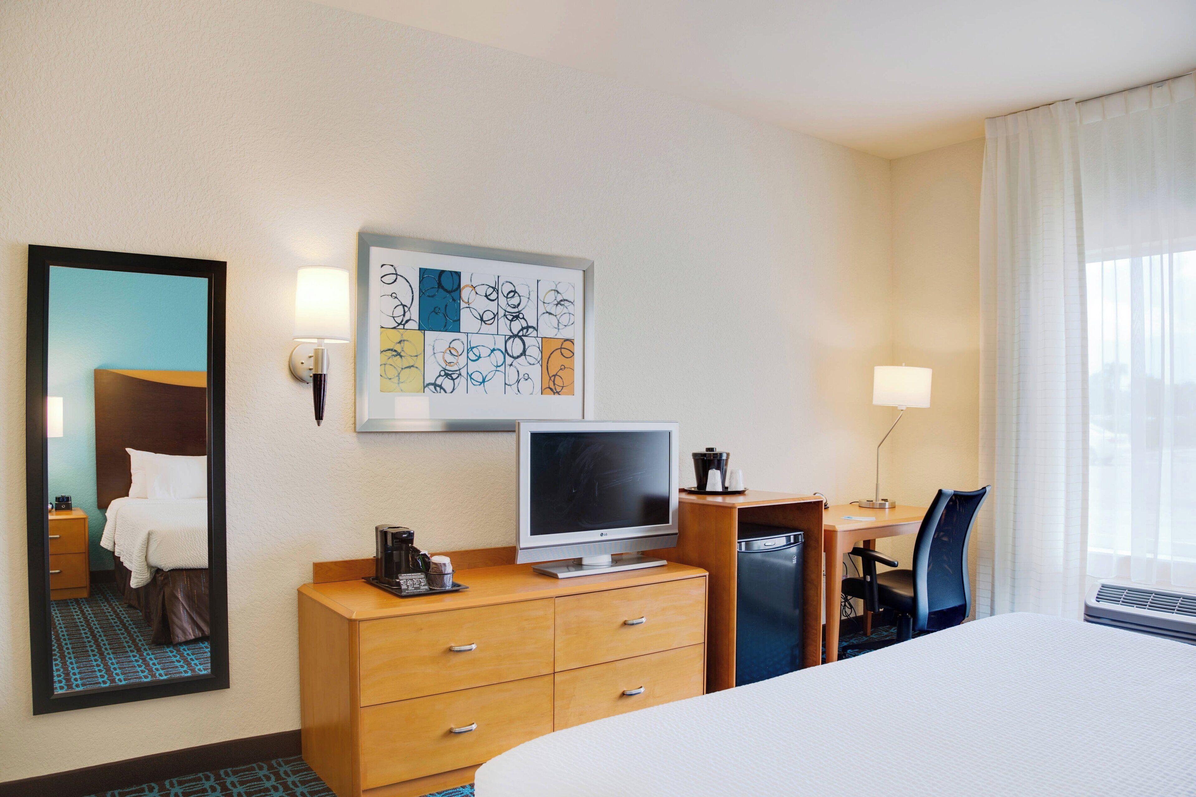 A hotel room with a bed, a desk, a television, a coffee maker, and a mirror.