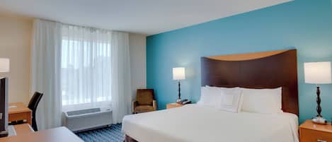 Ein Hotelzimmer mit einem großen Bett, zwei Nachttischen mit Lampen, einem Schreibtisch mit Stuhl, einem Fenster mit Vorhängen und einem Wandheizkörper.