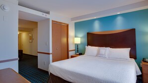 Una habitación de hotel con una cama grande, cabecera de madera, mesita de noche con lámpara y una pared azul decorativa.