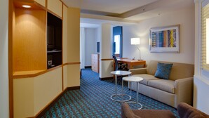 Habitación de hotel con kitchenette, sofá, una pequeña mesa redonda y un escritorio con lámpara.