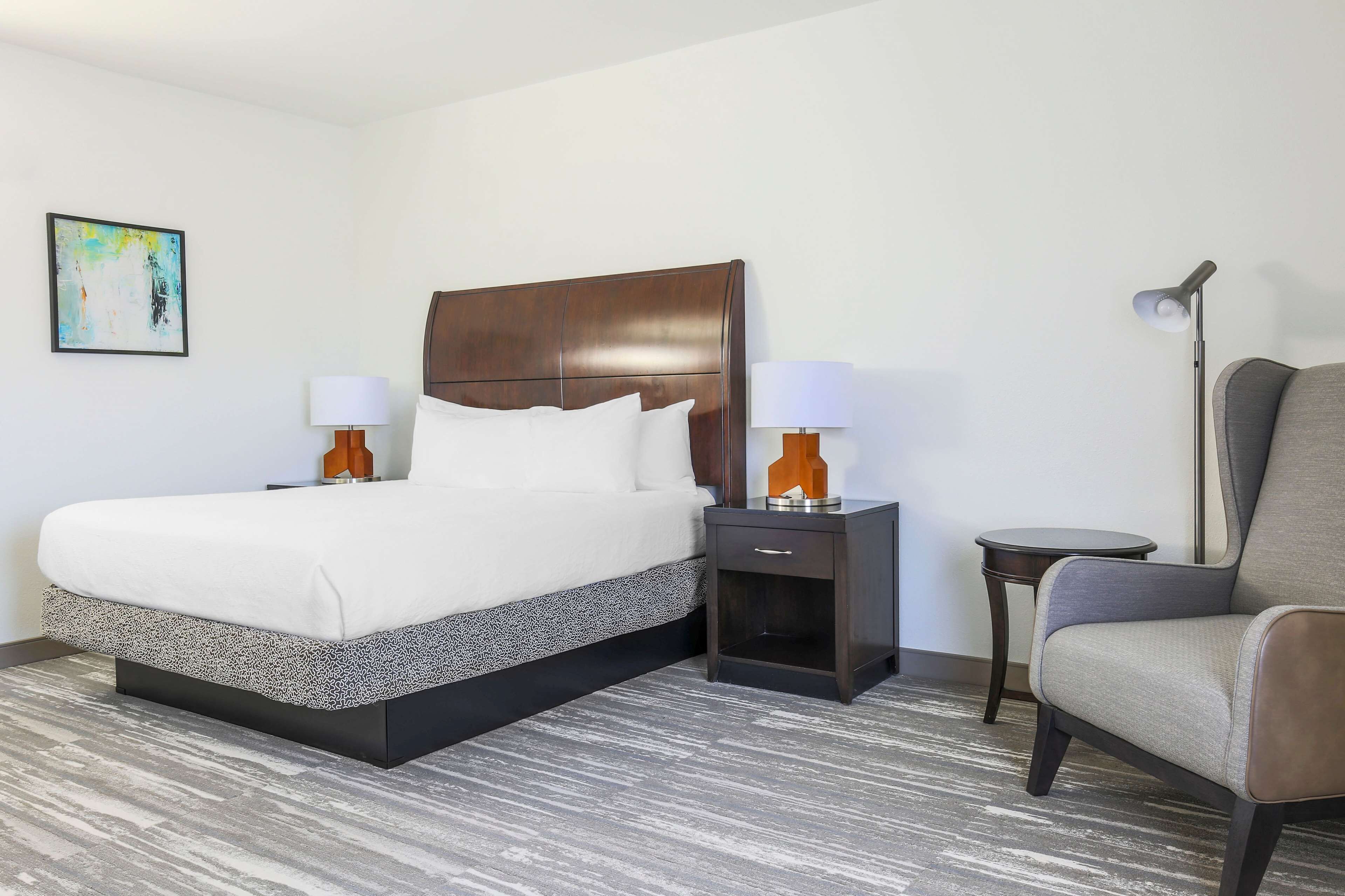 Une chambre d’hôtel avec un grand lit, deux tables de chevet avec des lampes, une chaise et une petite table.