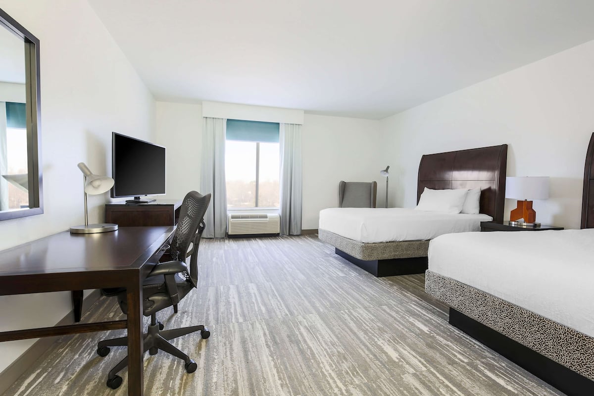 A hotel room with a desk, two beds, a TV, and a window with curtains.