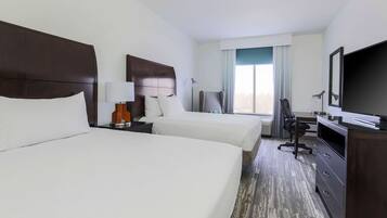 Une chambre d’hôtel avec deux lits, un bureau, une chaise, une télévision et une grande fenêtre.