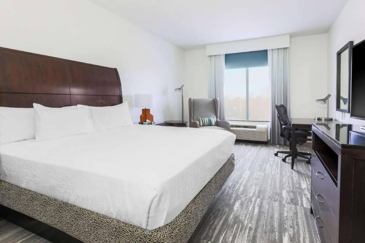 A hotel room with a large bed, a desk, a chair, a television, and a window with curtains.