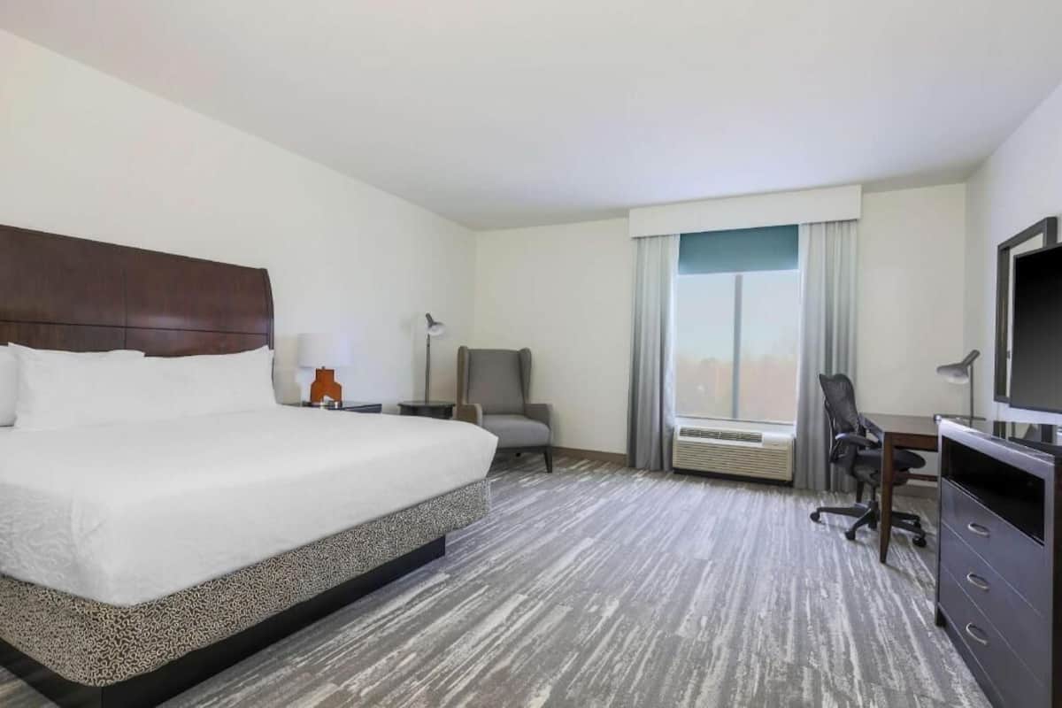A hotel room with a large bed, a desk, a chair, a television, and a window with curtains.