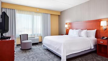 A hotel room with a large bed, a TV on a desk, a chair, and a desk lamp.