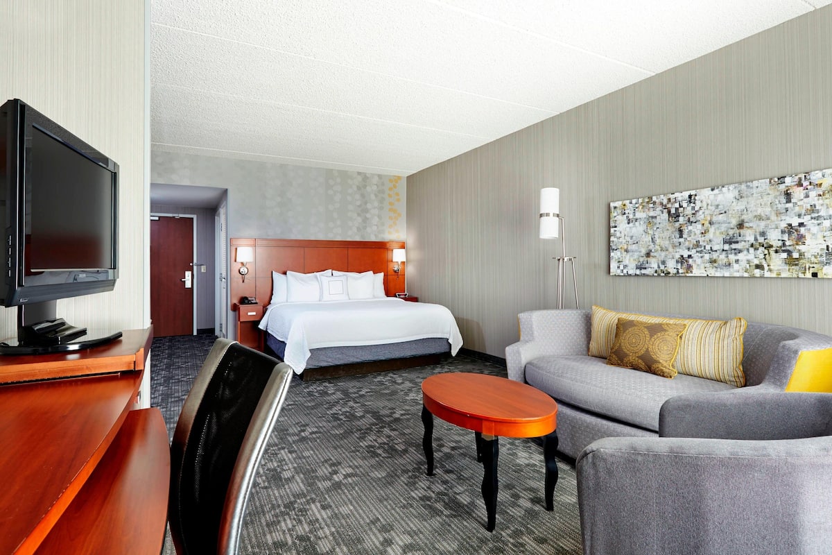 Una habitación de hotel con cama, sofá, televisión, escritorio y un cuadro en la pared.